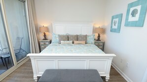 A bedroom with a large bed, two bedside tables with lamps, a bench, and a view of an outdoor area.