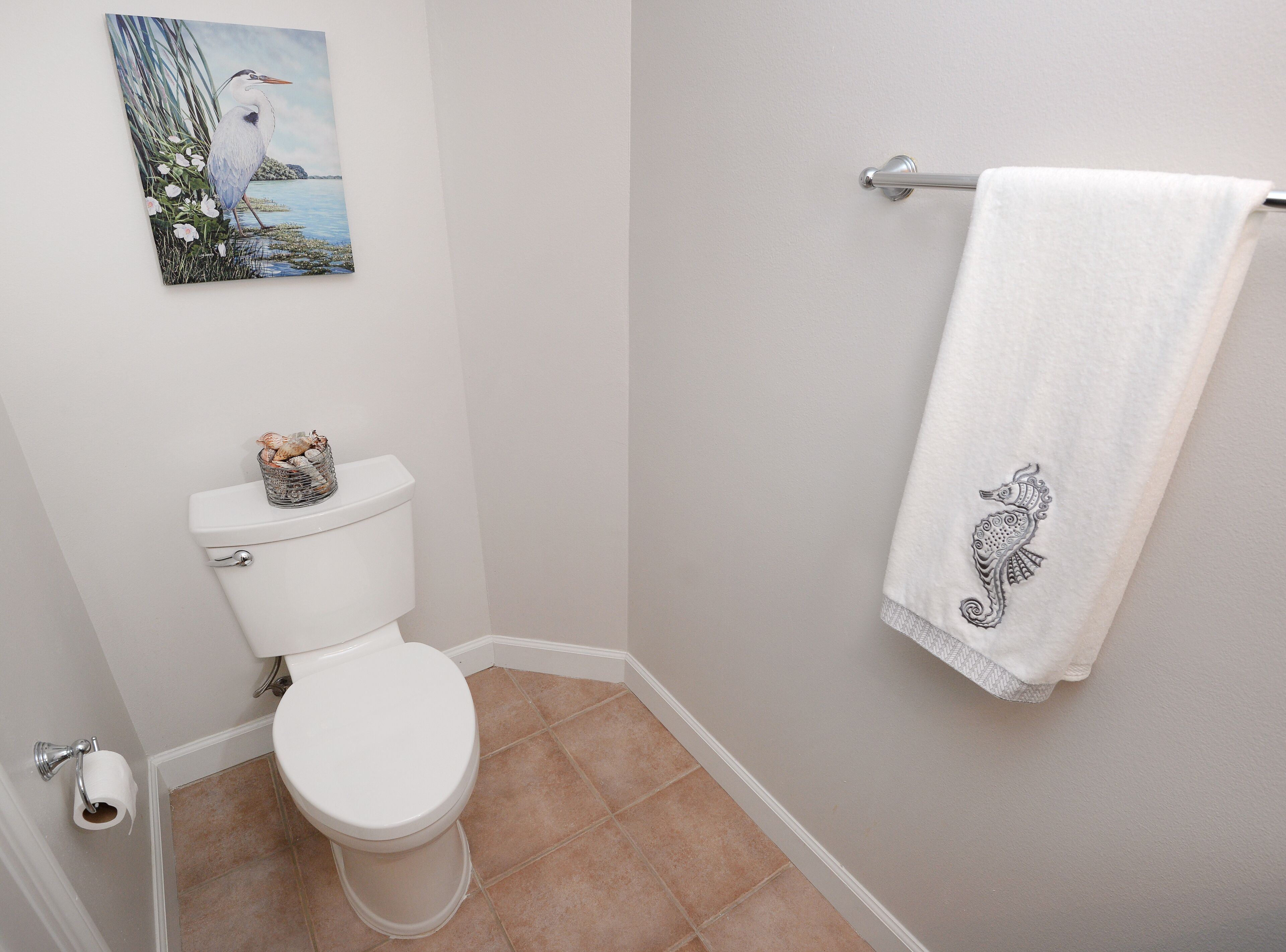 A bathroom with a toilet, a towel rack with a towel, and a painting on the wall.