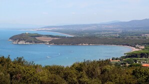 Paisagem costeira com uma praia, barcos e uma colina com um edifício.