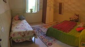 Quarto com duas camas, um guarda-roupa, uma janela e um tapete estampado.