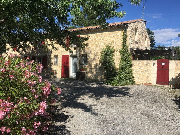 A stone building with a red door, a gravel driveway, and flowering plants. - Chalet with shaded terrace in a quiet location. (Tauriers)