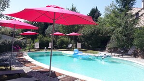 A swimming pool with red umbrellas, lounge chairs, and a dolphin inflatable.