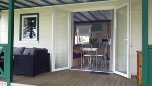 A covered outdoor area with a wicker sofa, a dining table with chairs, and a kitchen area visible through an open door.