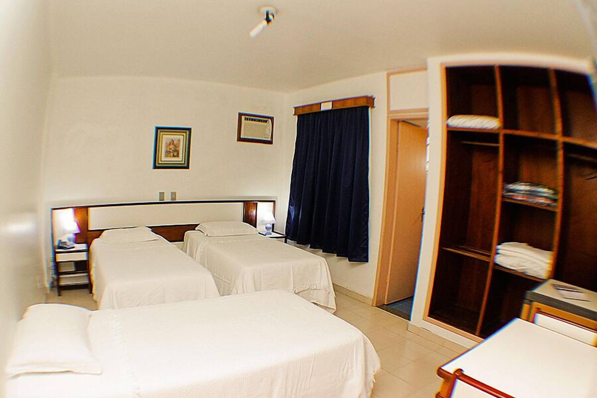 A hotel room with two beds, a desk, a wardrobe, and a door leading to another room.