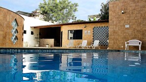A swimming pool with lounge chairs and a covered area with a tiled wall. - Shalako Hotel (Vitoria da Conquista)