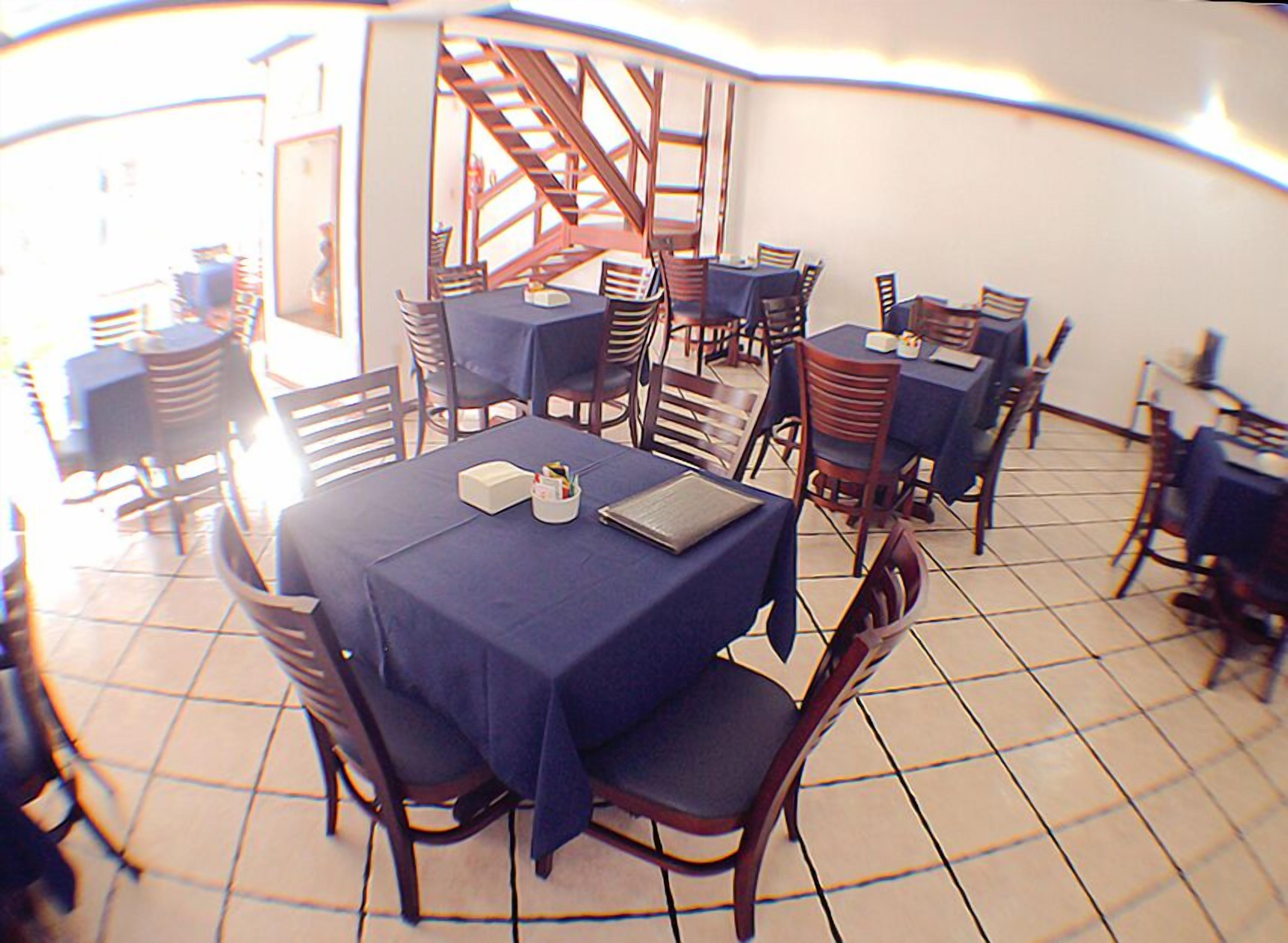 Un comedor con varias mesas y sillas, una escalera y suelo de baldosas.
