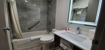 Un baño moderno con bañera, inodoro y lavamanos, que cuenta con una mampara de vidrio y un espejo sobre el lavamanos.