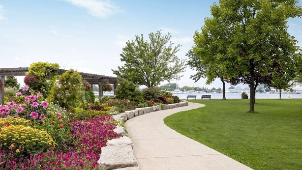 A landscaped pathway with a curved design, bordered by a stone edge, leading to a grassy area with a bench. - Super 8 by Wyndham SARNIA (Sarnia)