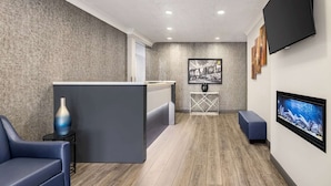 A modern reception area with a wooden floor, a reception desk, a blue sofa, a TV, and a framed picture on the wall. - Super 8 by Wyndham SARNIA (Sarnia)