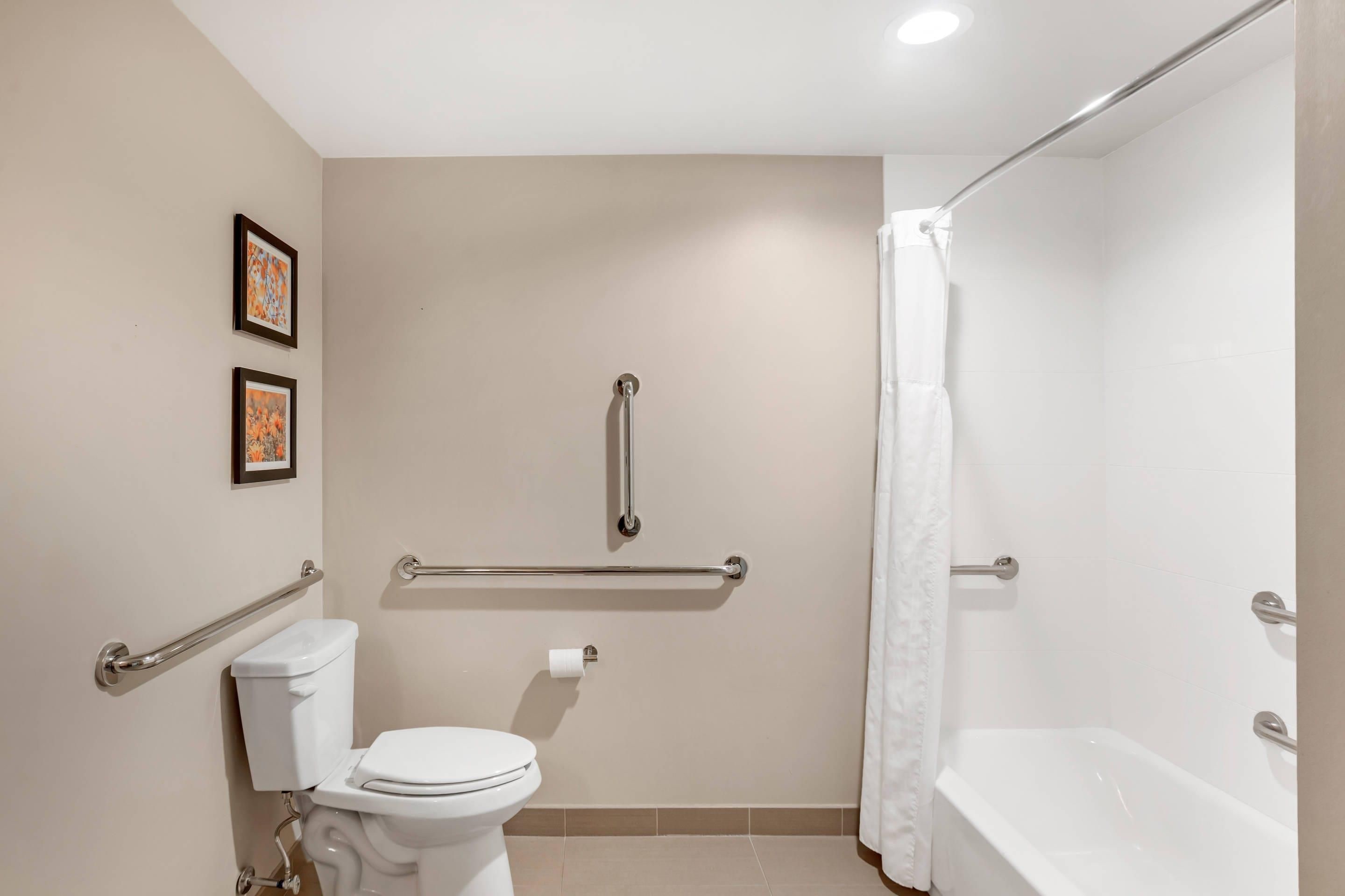 A bathroom with a toilet, a shower, and a bathtub. There are grab bars installed for safety.