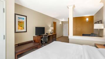 A hotel room with a bed, desk, chair, TV, and a framed picture on the wall.