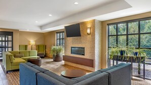 A modern lounge area with a flat-screen TV mounted on a textured wall, green sofas, a round coffee table, and potted plants. - Comfort Inn & Suites Gap Amish Country (Gap)