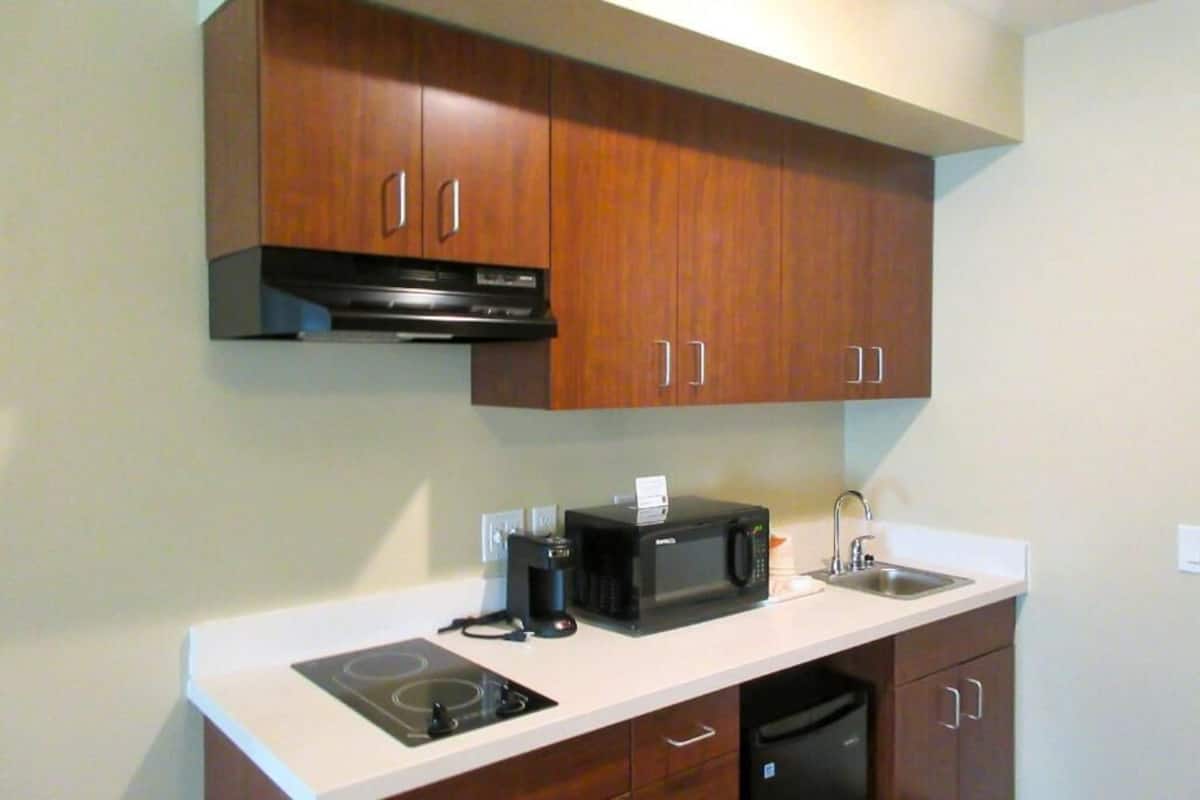 A compact kitchen with wooden cabinets, a microwave, a coffee maker, and a dishwasher.