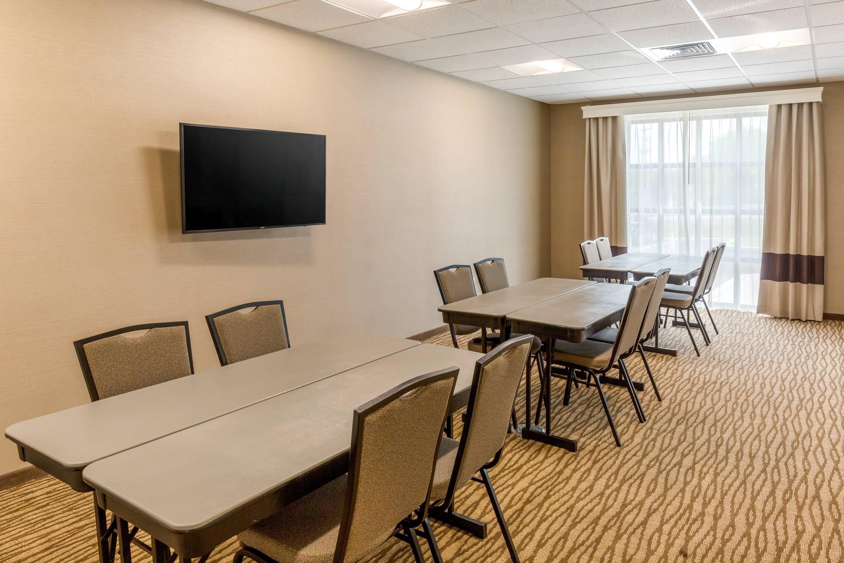 Un salón de conferencias con una pantalla plana, varias mesas y sillas.