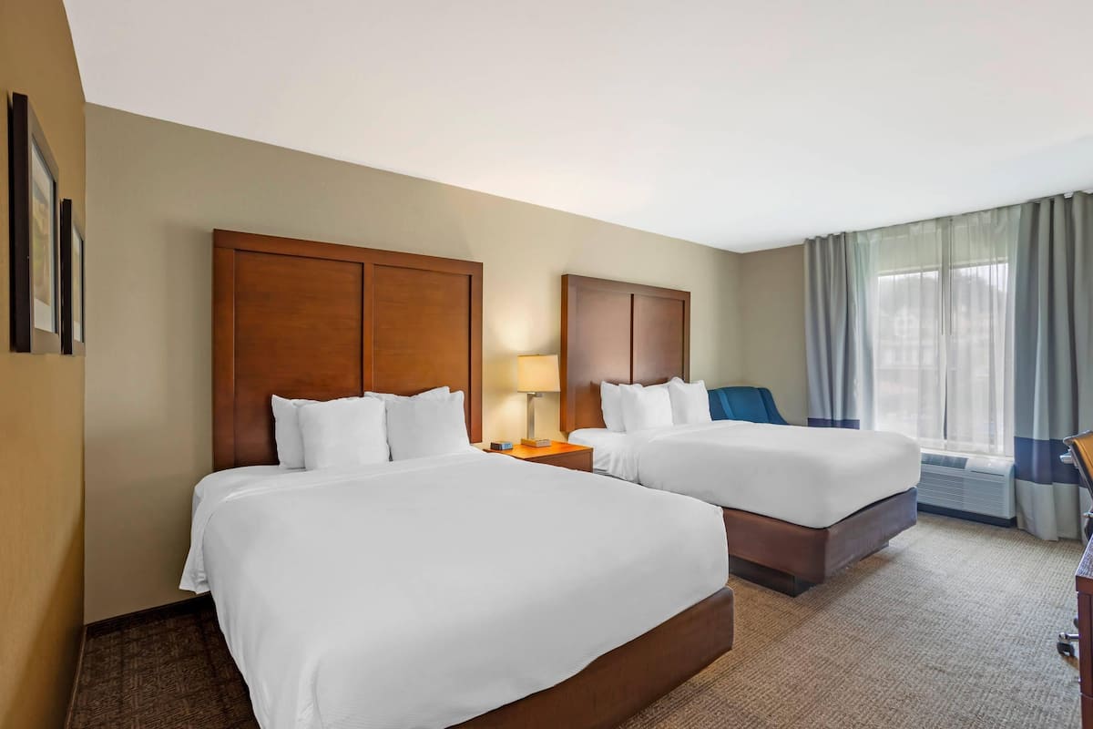 A hotel room with two beds, a desk, a chair, and a window with curtains.