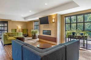 A modern lounge area with a flat-screen TV mounted on a textured wall, green sofas, a round coffee table, and potted plants. - Comfort Inn & Suites Gap Amish Country (Gap)