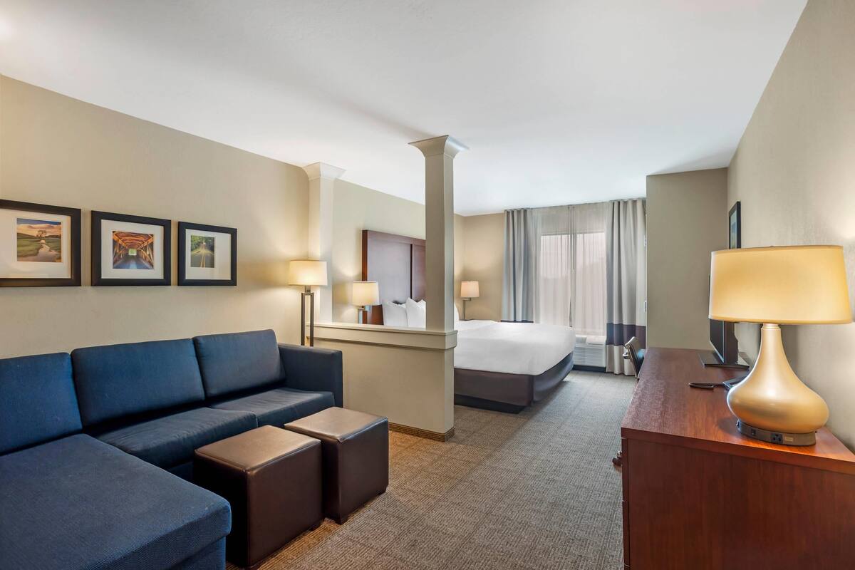 A hotel room with a sofa, a bed, a desk, and a lamp. There are three framed pictures on the wall.