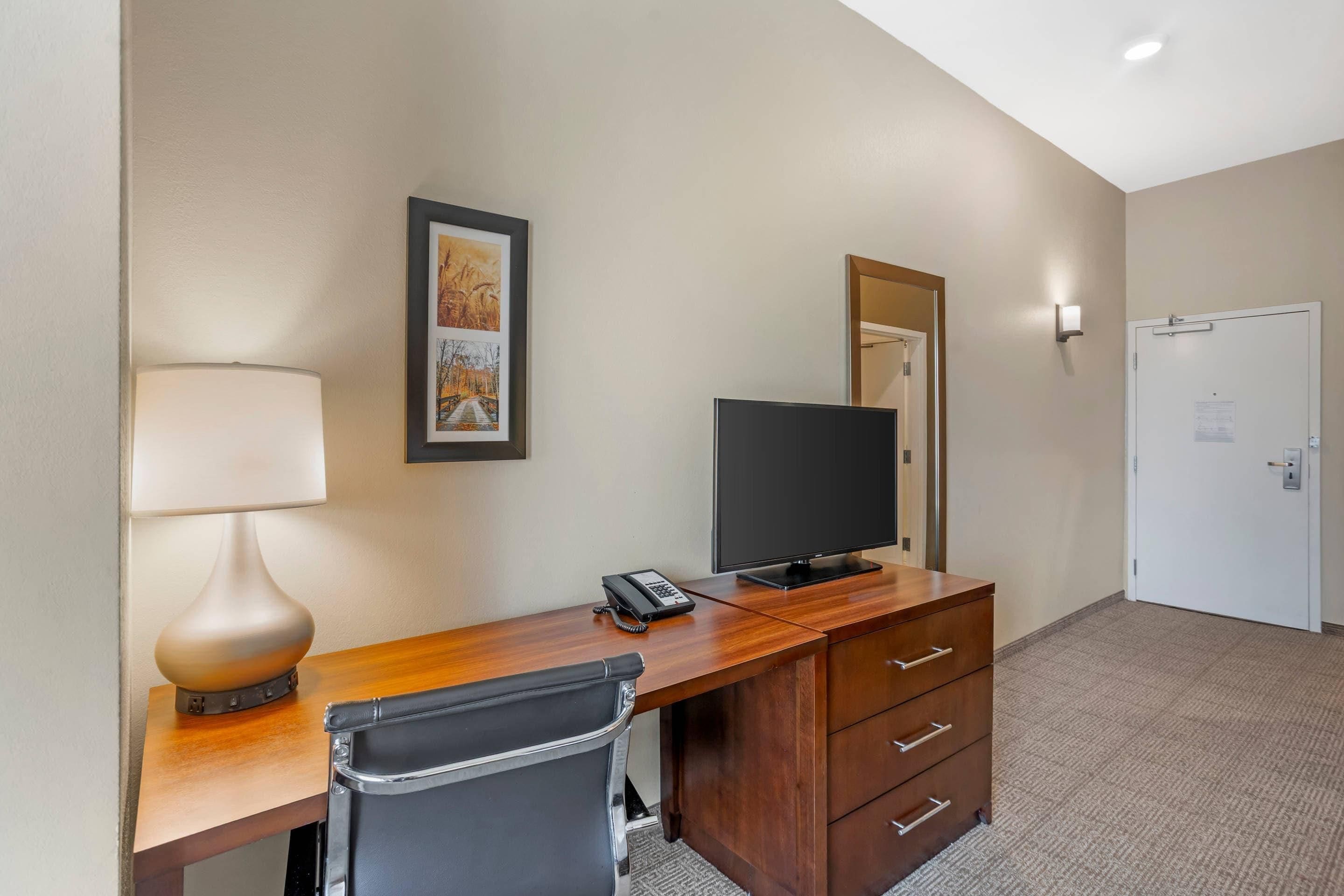 A hotel room with a wooden desk, a chair, a television, a telephone, and a framed picture on the wall.