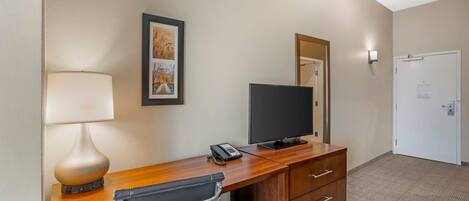 Quarto de hotel com escrivaninha de madeira, uma cadeira, televisão, telefone e um quadro na parede.