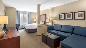 A hotel room with a bed, a blue sofa, a desk with a lamp, and framed pictures on the wall. - Comfort Inn & Suites Gap Amish Country (Gap)