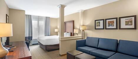 Une chambre d’hôtel avec un lit, un canapé bleu, un bureau avec une lampe et des tableaux encadrés au mur.