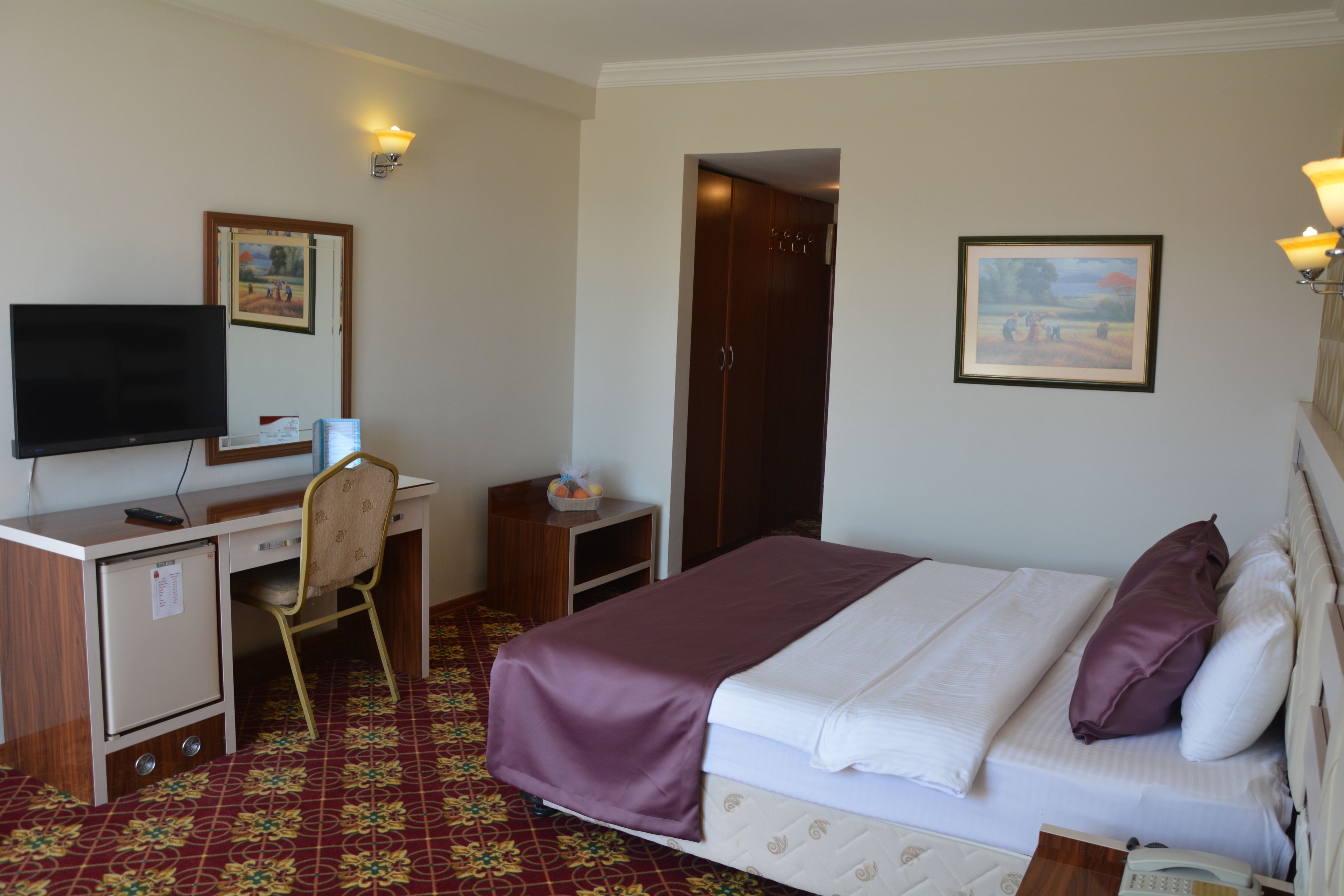 A hotel room with a bed, a desk with a computer, a chair, a television, and a wardrobe.