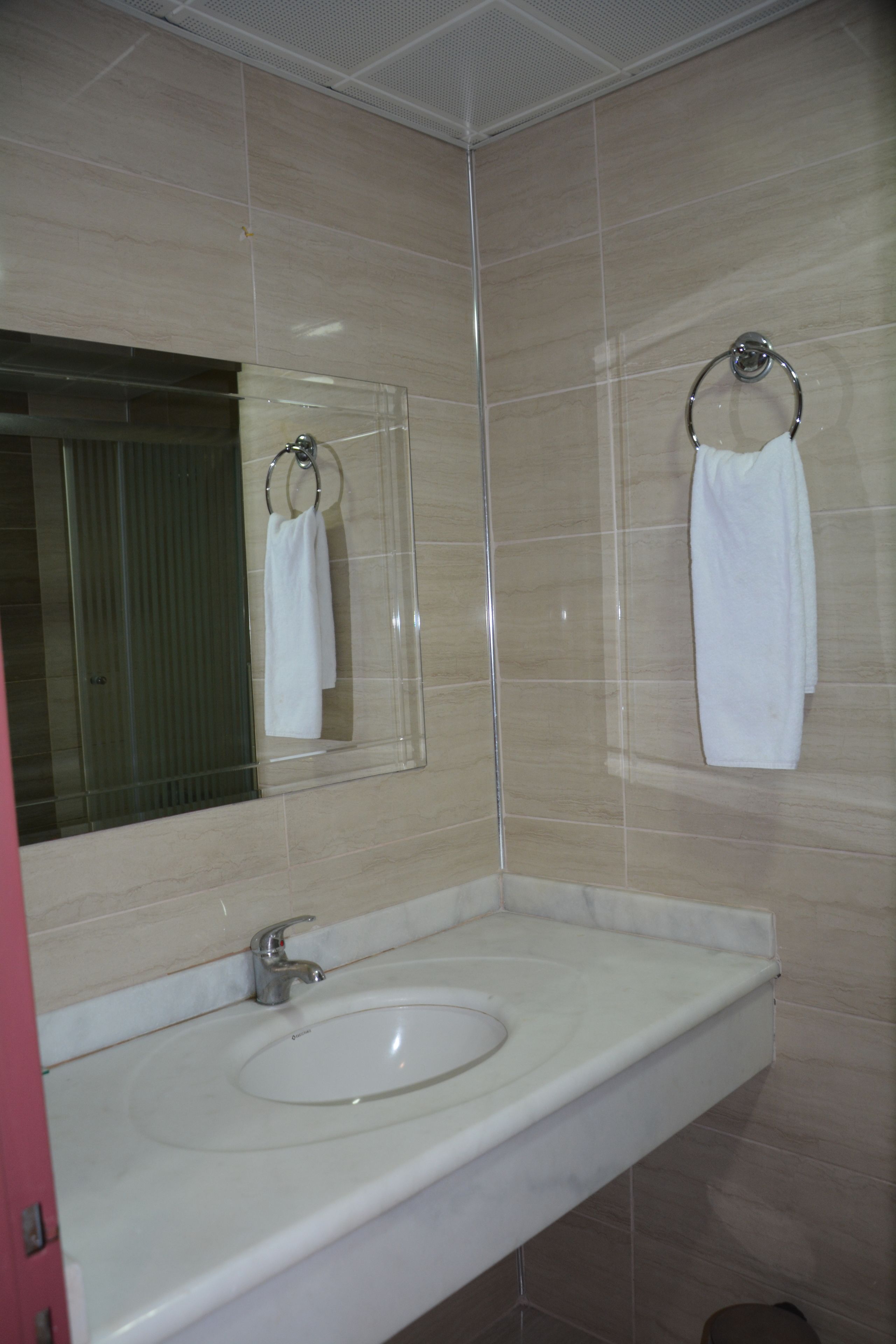 A bathroom with a white sink, a mirror, and two white towels hanging on towel rings.