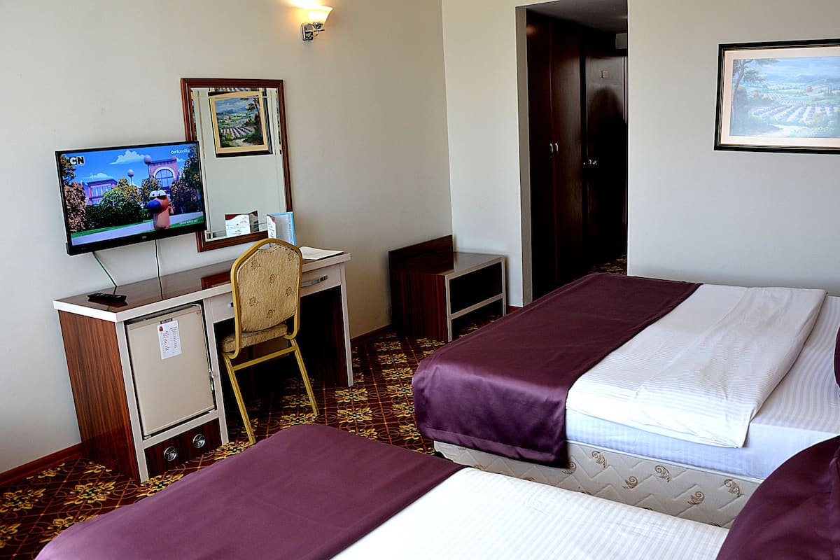 Een hotelkamer met twee bedden, een bureau met een computer, een televisie en een deur naar een andere kamer.