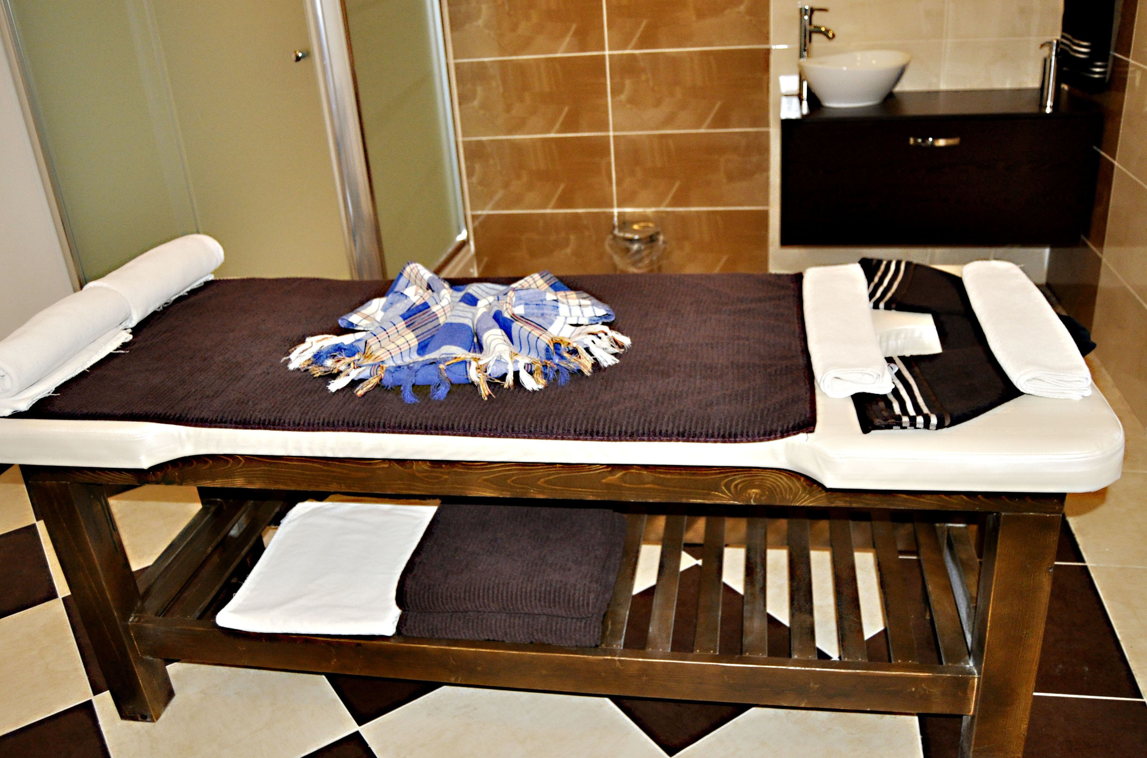 A wooden massage table with towels and a blue cloth in a bathroom with a tiled floor and a dark wooden vanity.