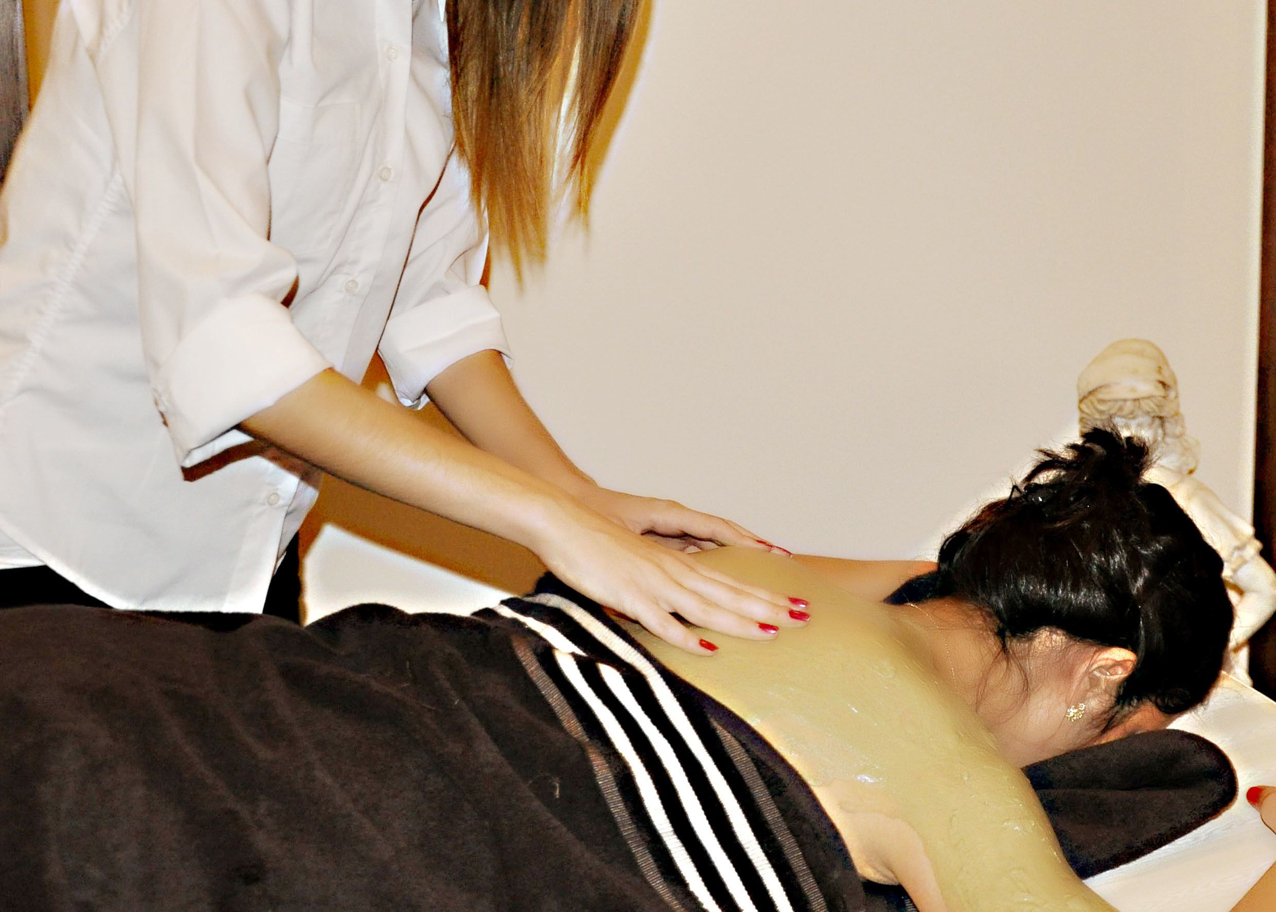 A person receiving a back massage in a room with a plain wall and a wooden floor.