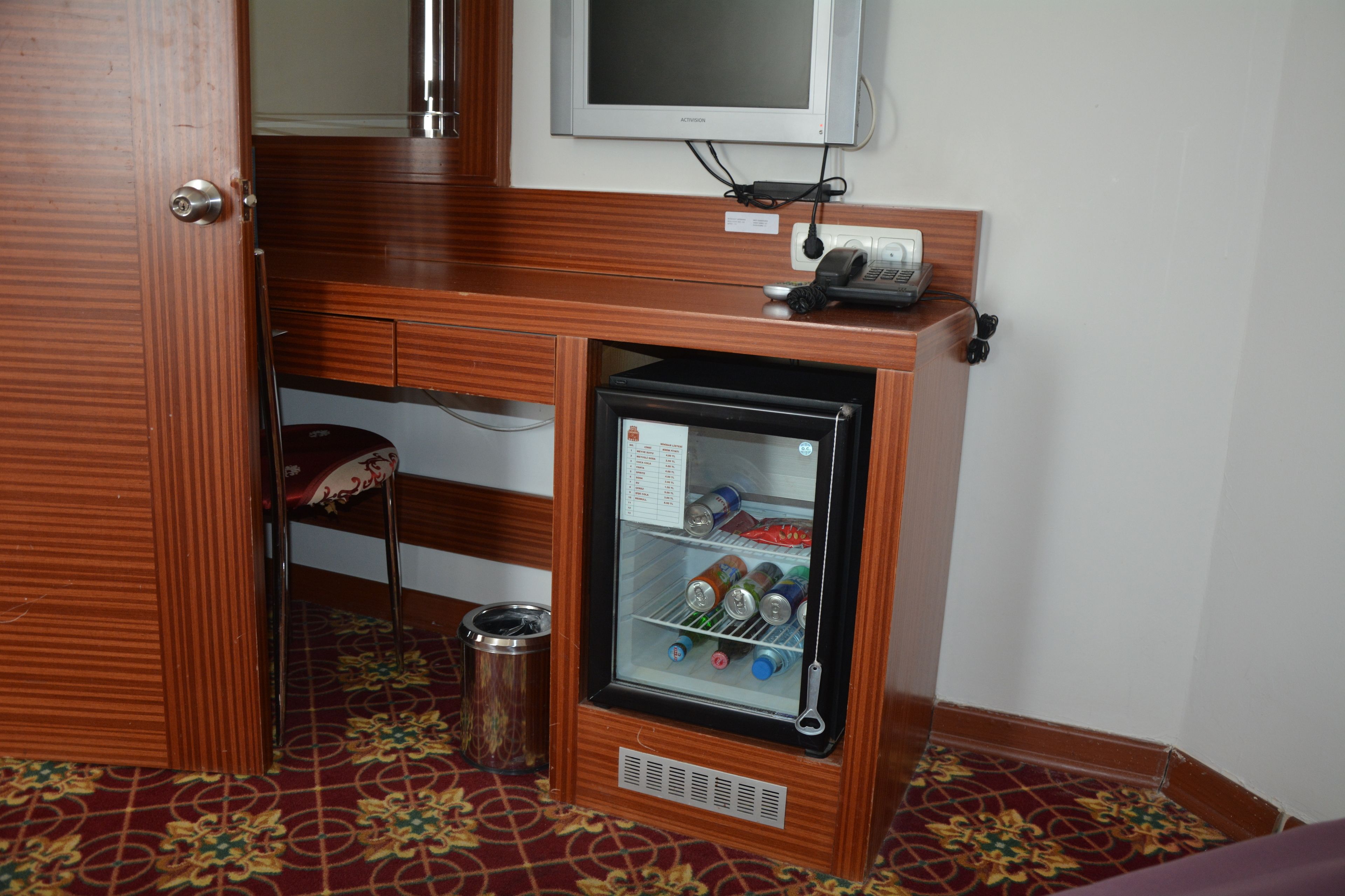 Un minibar compacto con un refrigerador, un bote de basura pequeño y un teléfono.