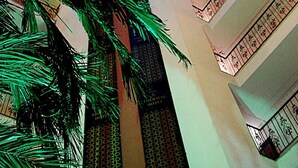 Een hotelinterieur met een glazen koepelplafond, zuilen en een patroonhekwerk op de balkons.