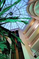Interior de un hotel con techo abovedado de cristal, columnas y barandilla con diseño en los balcones.