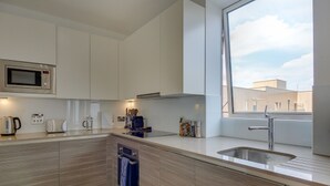 A modern kitchen with a built-in microwave, toaster, and coffee maker. It features a large window and a sink with a modern faucet. - Premium Hounslow Studio Apartments (Hounslow)
