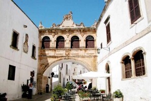 A narrow street with a stone archway, white buildings, and outdoor seating with umbrellas. - Swimming pool with sea view, historic center 700m, parking, 8' from the beaches (Ostuni)