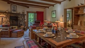 A cozy dining area with a wooden table set for four, benches with plaid cushions, a stone fireplace, and a view of the outdoors through a window.