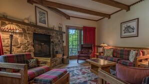 A cozy living room with a stone fireplace, plaid furniture, and a large window with red curtains.