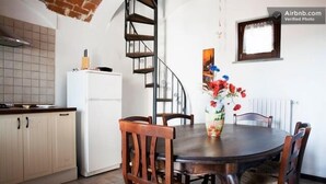Une cuisine avec un réfrigérateur blanc, des chaises en bois, une table de salle à manger ronde et un escalier en colimaçon.