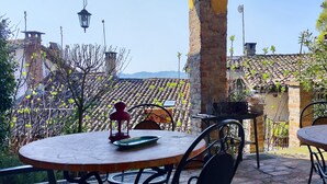 Un espace extérieur aménagé avec des tables rondes et des chaises en métal, entouré d’un mur de briques et de verdure.