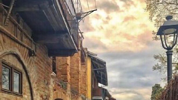 Une ruelle étroite pavée de pierres, bordée de bâtiments rustiques en briques, avec une porte en bois et un lampadaire.