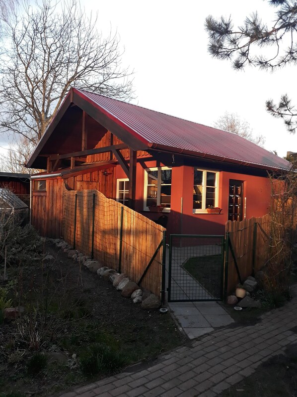 Cozy cabin with a prominent entrance and large window, surrounded by a wooden fence and stone pathway.