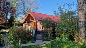 A wooden cabin with a red roof, surrounded by lush greenery and a stone pathway leading to the entrance. - Sunny holiday home with a cozy sleeping loft, idyllically located in the garden. (Barth)