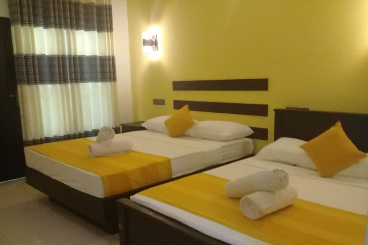 Ein Hotelzimmer mit zwei Betten, jeweils mit einer gelben Tagesdecke und weißen Kissen, sowie einem Nachttisch dazwischen.
