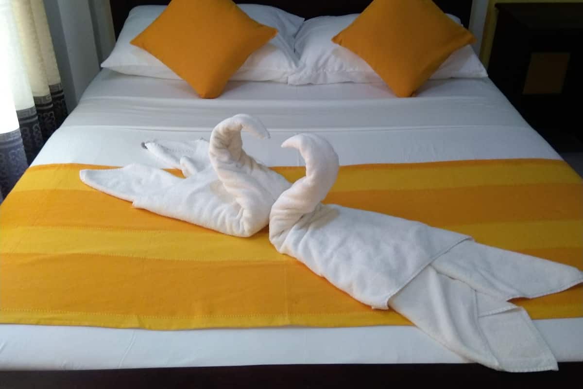 Ein Bett mit einer Schwan-Handtuch-Figur, zwei orangefarbene Kissen und einer gelb-gestreiften Tagesdecke.