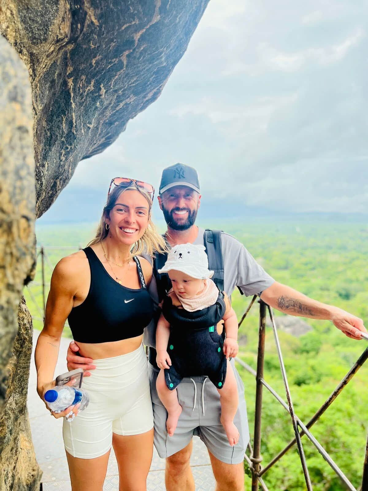 A family with a child on a rocky ledge with a view of a green landscape.