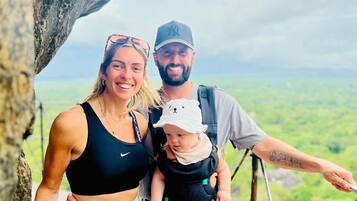 A family with a child on a rocky ledge with a view of a green landscape.