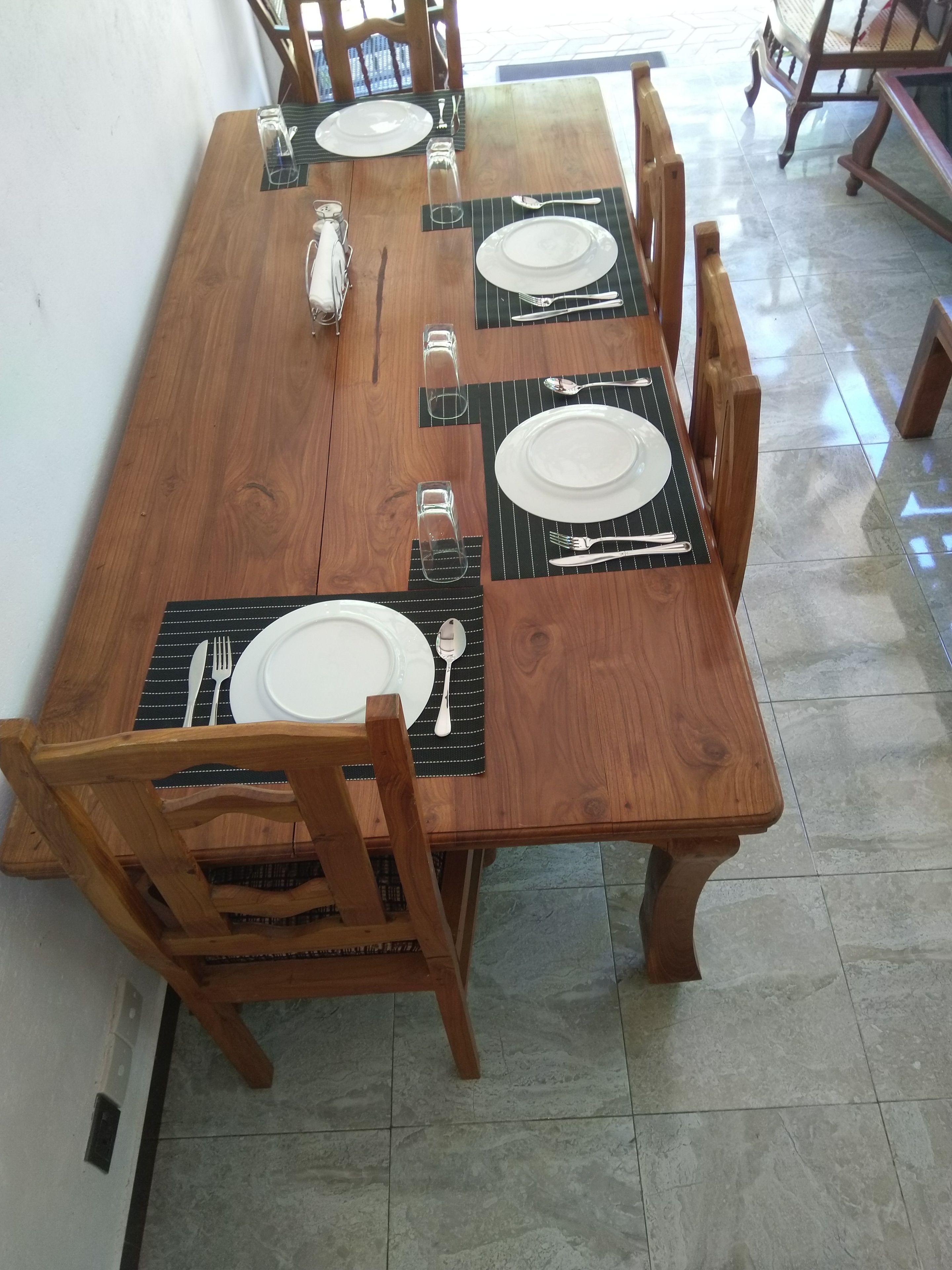 A wooden dining table set with plates, cutlery, and glasses, surrounded by wooden chairs.