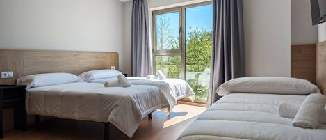 A hotel room with two beds, a wooden headboard, a nightstand, and a large window with curtains.