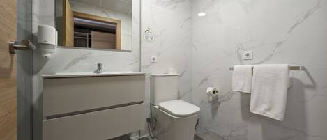 A modern bathroom with a marble wall, a toilet, a sink with a mirror, and a towel rack.