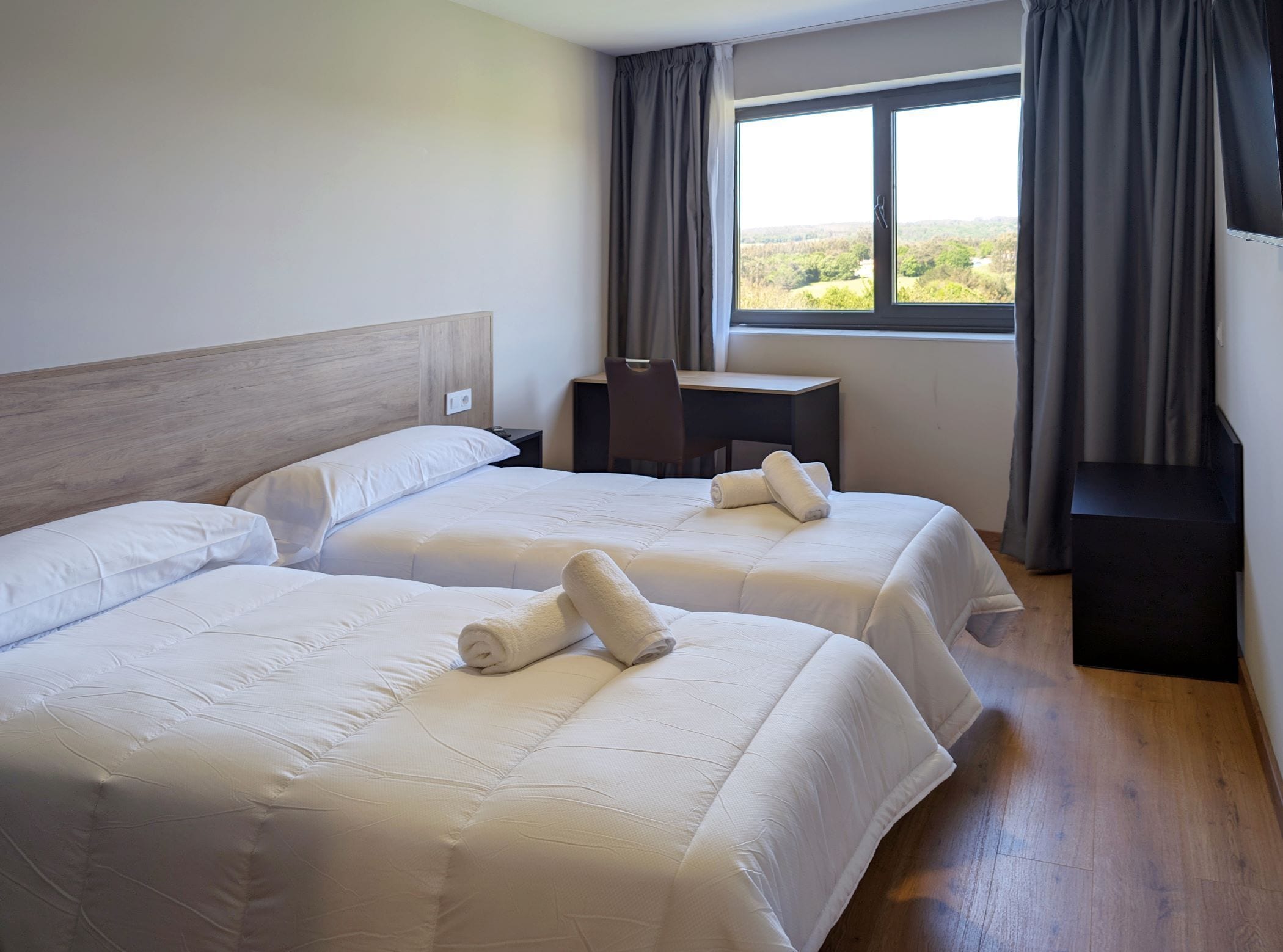 Habitación de hotel con dos camas, un escritorio y una ventana con cortinas.